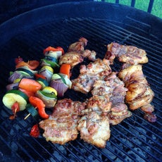 Chicken thighs and vegetable skewers cooking on a charcoal grill